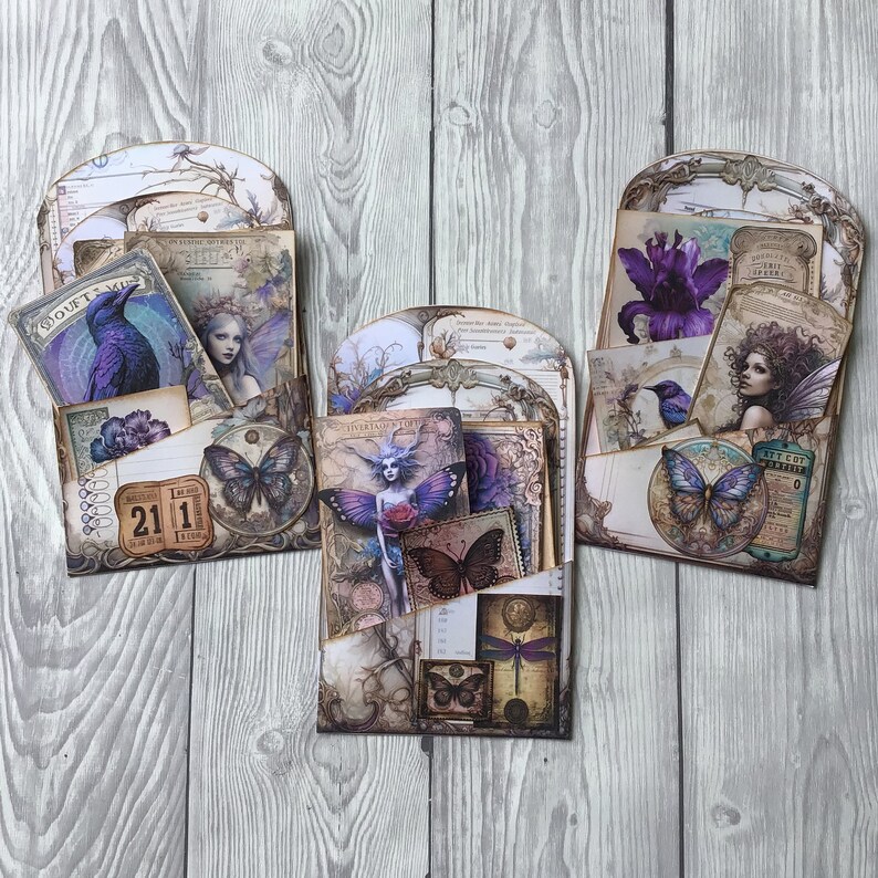 Puede incluir: Tres organizadores de bolsillo de papel decorativos con un tema de hadas vintage. Cada bolsillo presenta ilustraciones de hadas, mariposas y flores en tonos morados, azules y crema. Los bolsillos est&aacute;n llenos de tarjetas y etiquetas m&aacute;s peque&ntilde;as.