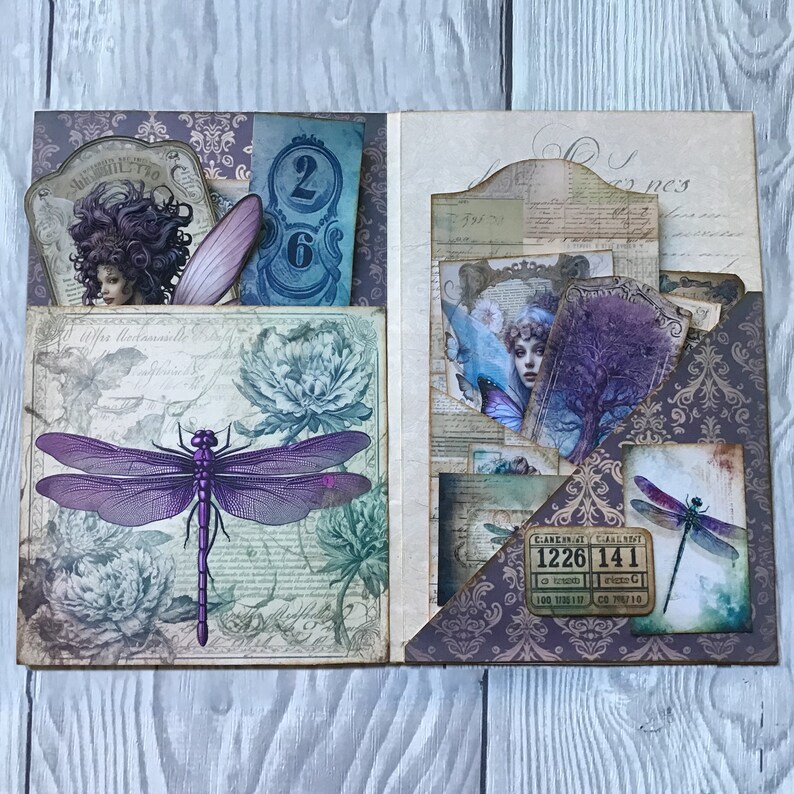 Puede incluir: Scrapbook abierto con un dise&ntilde;o de lib&eacute;lula p&uacute;rpura, detalles florales y elementos ef&iacute;meros vintage. Las p&aacute;ginas presentan bolsillos que contienen tarjetas con im&aacute;genes de mujeres, n&uacute;meros y boletos. La paleta de colores incluye p&uacute;rpura, azul y crema.