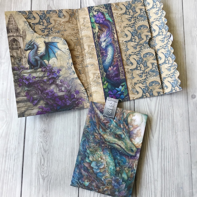 May include: A blue and gold dragon with intricate details is featured on the cover of a journal. The journal is open to reveal a patterned interior with a silver bookmark.