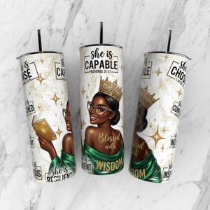 Puede incluir: Tres vasos aislados blancos y dorados con pajitas negras. Cada vaso presenta un retrato de una mujer negra con corona y gafas, con texto inspirador. El texto incluye "She is Capable", "Blessed with Wisdom" y otras afirmaciones.