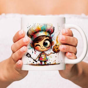 May include: White ceramic mug featuring a cartoon chef girl with a colorful chef's hat and apron. The illustration includes a cookie and a spatula. The mug is held by hands.