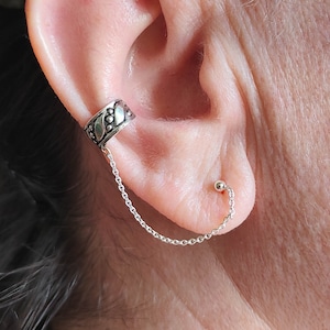 Puede incluir: Un pendiente de aro de plata con una cadena que se conecta a un pequeño pendiente de bola de plata.