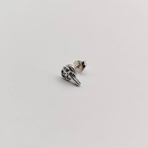 May include: Silver axe earring with a detailed design. The earring is a stud style with a post and a butterfly backing.