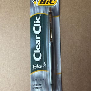 May include: A black BIC Clear Clic pen in its original packaging. The pen has a silver barrel with a gold-colored tip and clip. The packaging is a clear plastic blister pack with the BIC logo and product information.