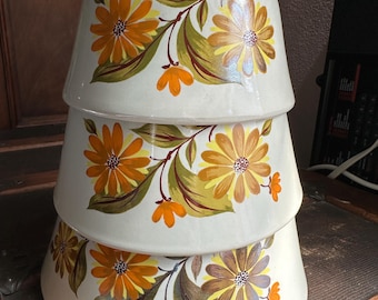May include: Stacked set of three off-white ceramic mixing bowls. Each bowl is decorated with a floral pattern featuring orange and yellow flowers, green leaves, and brown stems. The bowls are nested together, showcasing the decorative design.