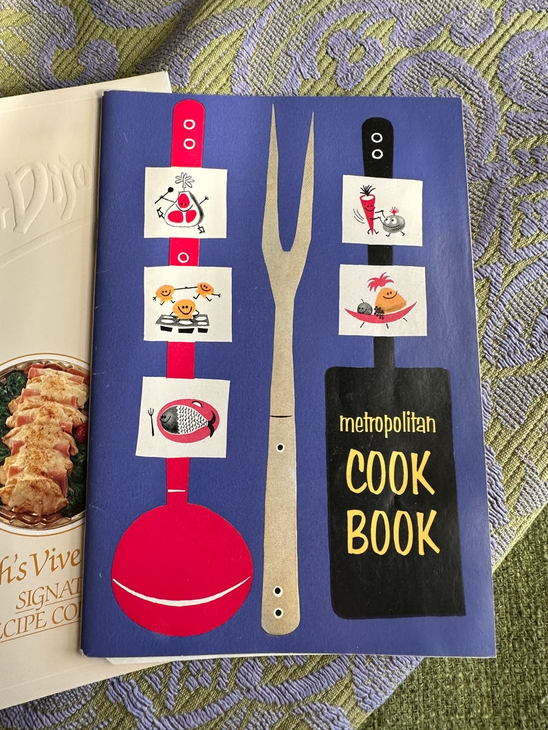 May include: A blue cookbook with the title "Metropolitan Cook Book" in yellow letters. The cover features illustrations of a fork, a ladle, and various food items.