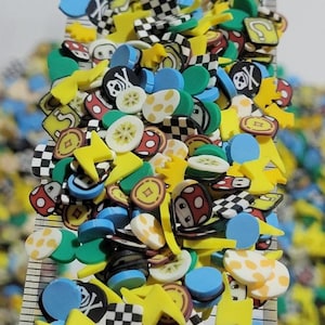 May include: A collection of colorful, small, decorative embellishments. The assortment includes yellow lightning bolts, blue circles, red and white mushrooms, black and white checkered shapes, and other game-themed designs. A ruler is visible in the background.