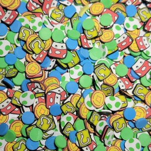 May include: A collection of colorful, flat, plastic charms featuring iconic video game characters and items. The charms include green question blocks, red mushrooms, gold coins, and green and white eggs.