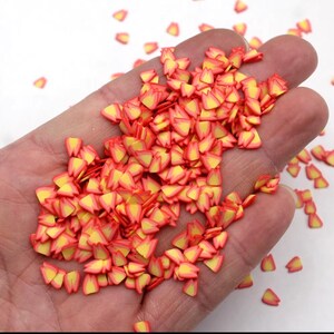 May include: A handful of small, flame-shaped polymer clay pieces. Each piece has a yellow center and red-orange edges, resembling tiny flames. These decorative elements are likely used for crafting or jewelry making.