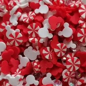 May include: A close-up of a mix of red, white, and clear decorative elements. The image features red Mickey Mouse shapes, red and white peppermint candies, and clear rhinestones. These elements are scattered throughout the image.