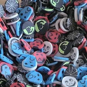 May include: A collection of colorful Halloween-themed polymer clay beads. The beads feature various designs, including spiderwebs, ghosts, skulls, and jack-o'-lanterns. The color palette includes black, white, red, blue, and green, creating a festive and spooky aesthetic.