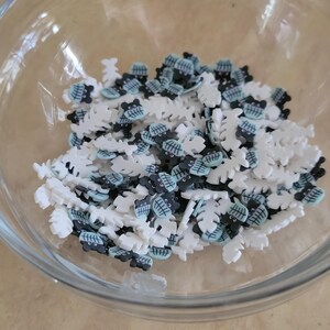 May include: A bowl filled with white and black sprinkles shaped like leaves and bears. The bears have black eyes and a blue and white striped pattern.