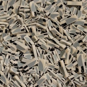 May include: A pile of miniature knife-shaped polymer clay pieces. Each piece features a white handle, a gray blade, and a black accent. The small size and uniform design suggest they are intended for crafting or decorative purposes.