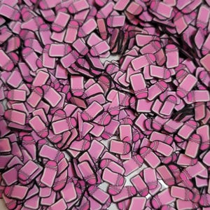 May include: A pile of pink polymer clay sprinkles shaped like pink and white pencils with black outlines. The sprinkles are in various shades of pink and are scattered across the surface.