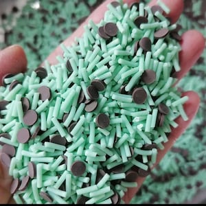May include: A close-up of a handful of green and brown sprinkles. The sprinkles are a mix of long, thin green pieces and small, round brown pieces.