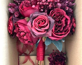 May include: A burgundy bridal bouquet with a matching buttonhole. The bouquet features roses, berries, and greenery. The buttonhole is a single rose with berries and greenery.