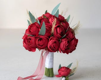 May include: A bridal bouquet of deep red roses, complemented by green foliage and fine sprigs. The bouquet is wrapped in white fabric and has a flowing red ribbon. A matching buttonhole is also present.