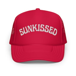 May include: A red trucker hat with a white mesh back. The front of the hat has the word "SUNKISSED" embroidered in white.