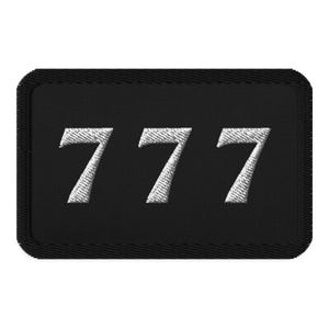 May include: Black rectangular patch with the number 777 embroidered in white. The patch has a black border and a textured appearance, suggesting it is made of fabric.