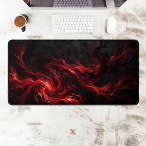 May include: A large rectangular desk mat with a swirling red and black abstract design. The pattern resembles fire or smoke. The mat is on a white desk with a keyboard, mouse, and coffee cup visible.