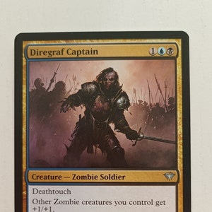 May include: A Diregraf Captain Magic: The Gathering card featuring a zombie soldier with a sword. The card is gold and blue with a 2/2 power and toughness. The card text reads "Deathtouch. Other Zombie creatures you control get +1/+1. Whenever another Zombie you control dies, target opponent loses 1 life. Though its mind has long since rotted away, it wields a sword with deadly skill."