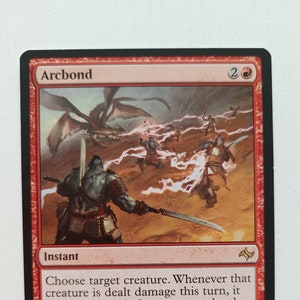 May include: A red Magic: The Gathering card with the name "Arcbond" and the text "Choose target creature. Whenever that creature is dealt damage this turn, it deals that much damage to each other creature and each player." The card features an illustration of a red-skinned creature with a sword, surrounded by other creatures and lightning.