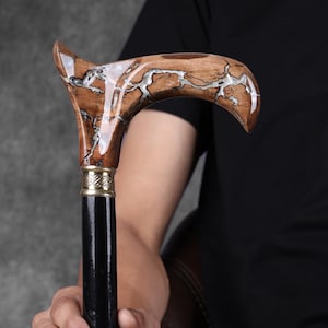 May include: A wooden walking stick with a brown and white marbled design. The handle is curved and has a brass accent. The stick is black below the handle.