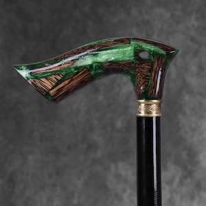 Puede incluir: Bastón artesanal con un diseño único. El mango presenta un mosaico de madera y resina verde, con una banda dorada en la parte superior del eje negro. Un accesorio elegante.