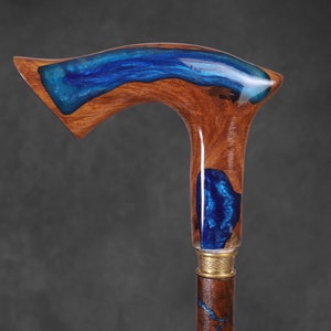 May include: A wooden walking stick with a blue resin inlay. The handle is curved and has a gold metal band.