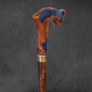 May include: A wooden walking stick with a blue resin handle. The handle is shaped like a crook and has a gold band around the bottom.