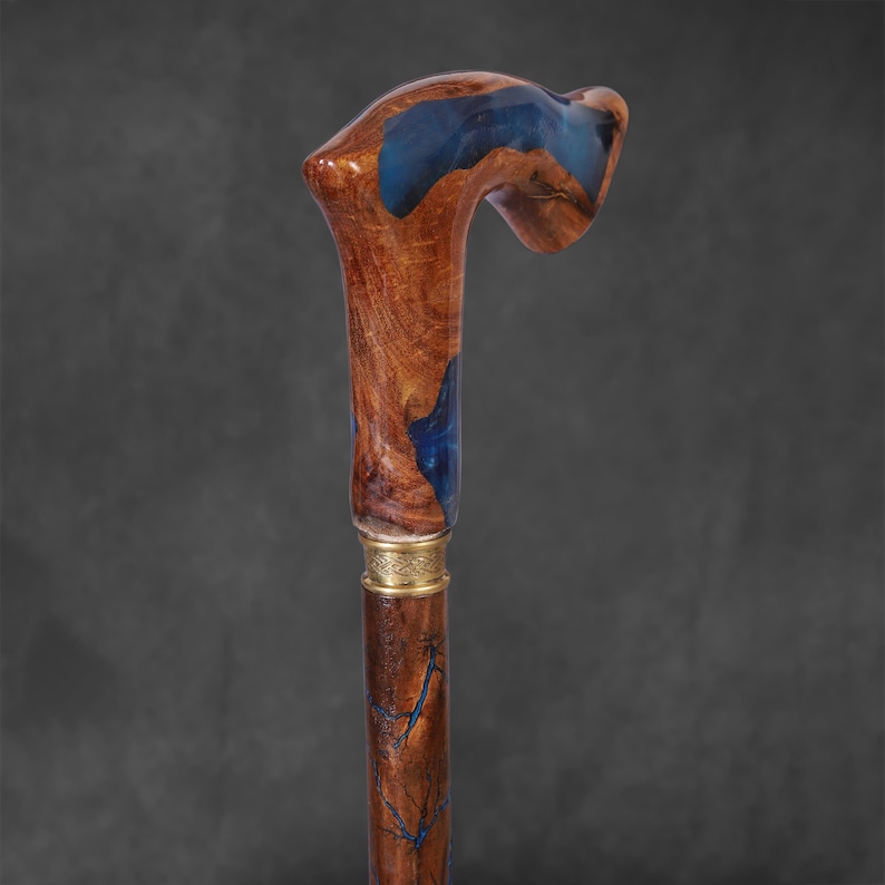 May include: A wooden walking stick with a blue resin handle. The handle is shaped like a crook and has a gold band around the bottom.
