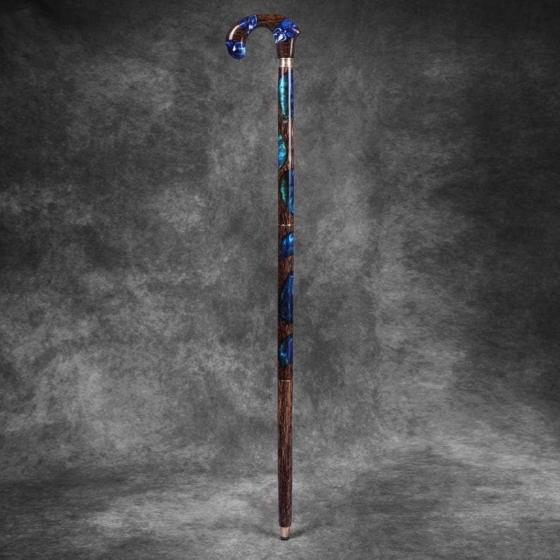 May include: A decorative walking cane with a curved handle and a dark wood shaft. The handle and shaft feature blue and teal accents. The cane is approximately 36 inches long.