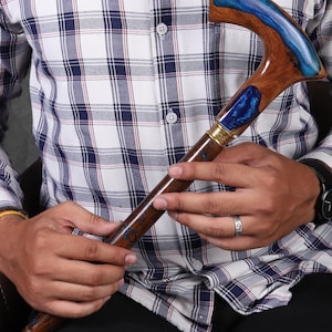 May include: A wooden walking stick with a blue and brown resin handle. The handle is shaped like a hook and has a gold accent.