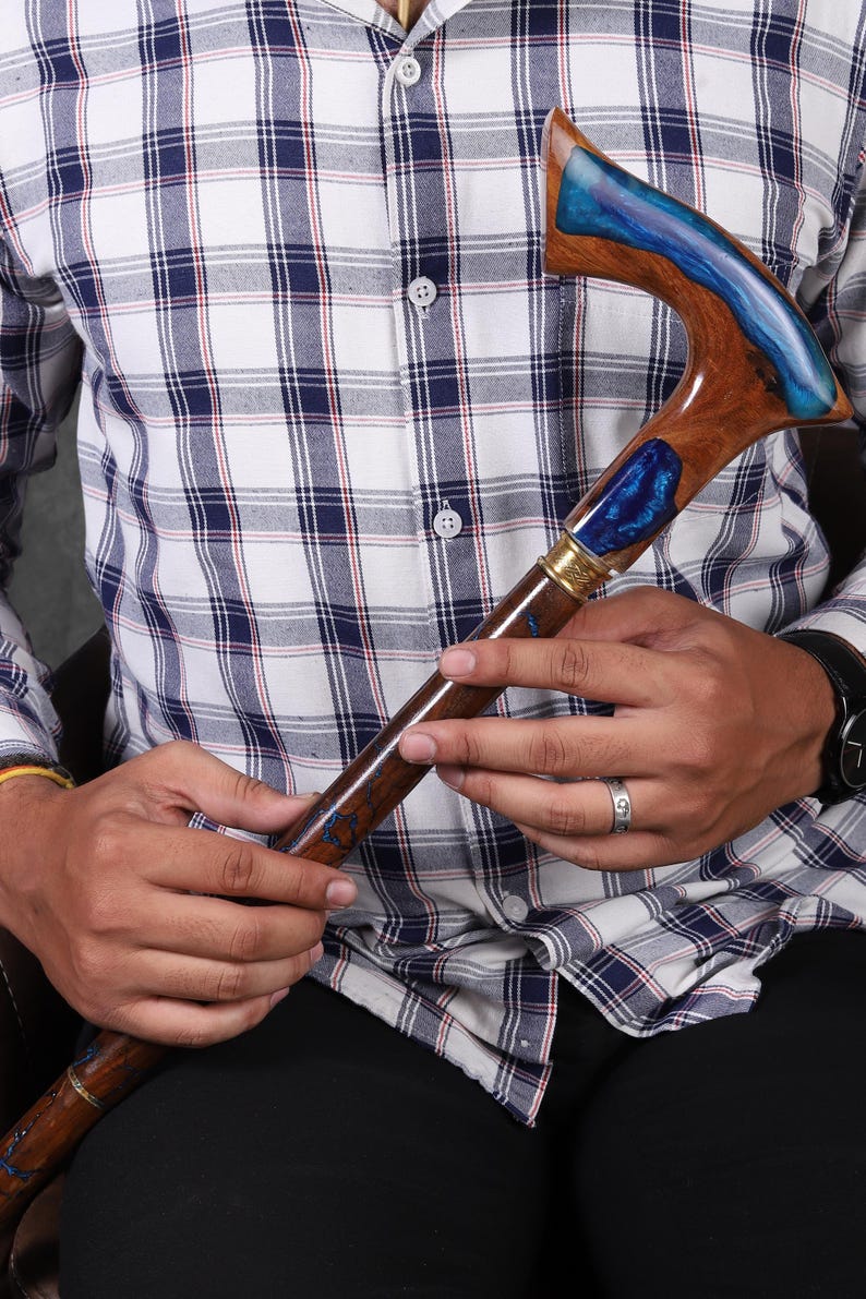 May include: A wooden walking stick with a blue and brown resin handle. The handle is shaped like a hook and has a gold accent.