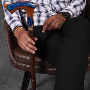 May include: A wooden walking stick with a blue and brown resin handle. The handle has a unique, curved design.