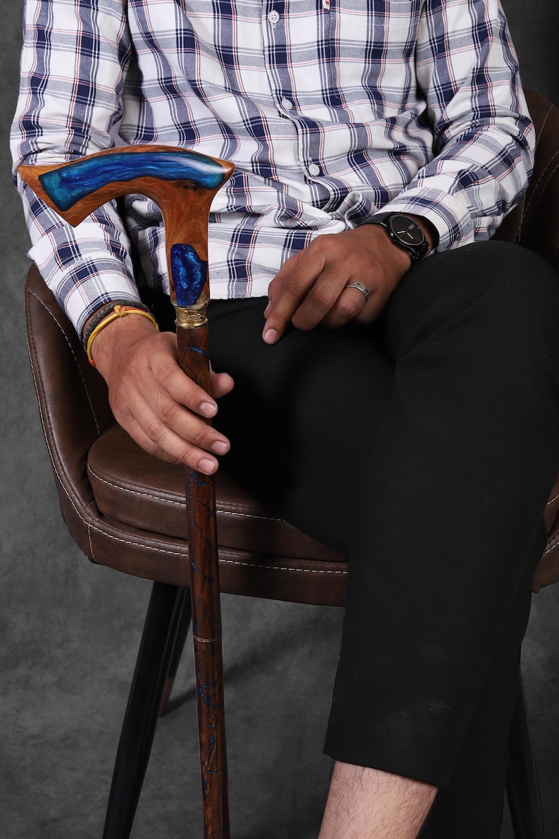 May include: A wooden walking stick with a blue and brown resin handle. The handle has a unique, curved design.
