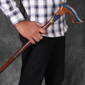 May include: A wooden walking stick with a blue and brown resin handle. The handle is curved and has a gold accent.