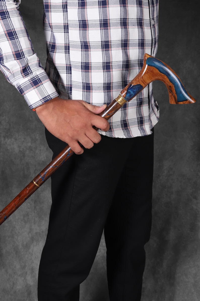 May include: A wooden walking stick with a blue and brown resin handle. The handle is curved and has a gold accent.