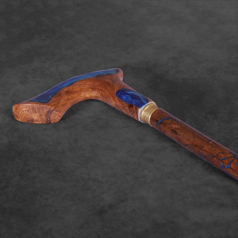 May include: A wooden walking stick with a blue resin inlay. The handle is curved and the stick is brown with a gold accent.