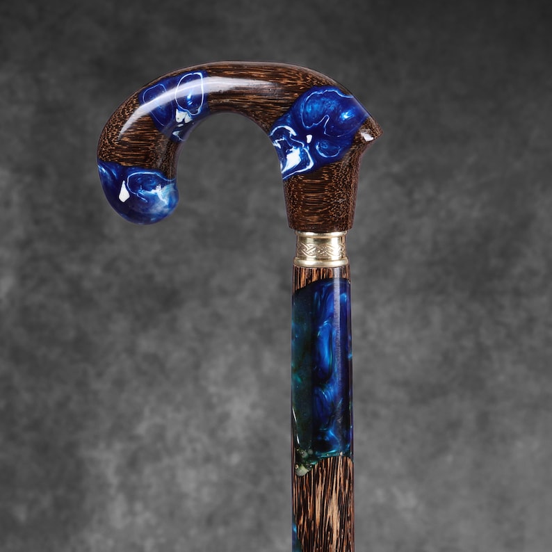 May include: A handcrafted walking cane with a curved handle. The handle and upper shaft are dark wood inlaid with blue and white resin. The lower shaft has a silver band and a blue and green resin design.