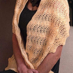 May include: A light yellow crocheted shawl with a delicate openwork pattern. The shawl is draped over the shoulders, creating a soft, textured look. The design features a scalloped edge and is made of a soft, lightweight yarn.