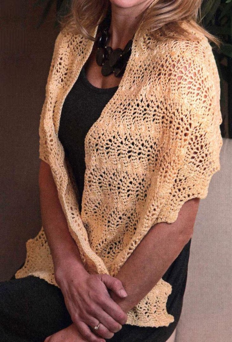 May include: A light yellow crocheted shawl with a delicate openwork pattern. The shawl is draped over the shoulders, creating a soft, textured look. The design features a scalloped edge and is made of a soft, lightweight yarn.