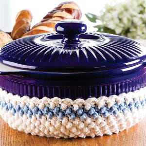 Puede incluir: Una cacerola de cerámica azul con tapa blanca y un posavasos de ganchillo blanco y azul.