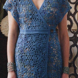 May include: A blue crocheted wrap dress with a V-neckline and a button closure. The dress has a delicate lace pattern and a flowing silhouette.