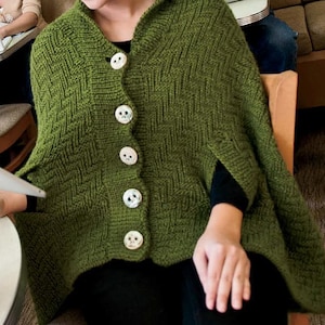 May include: A green knitted hooded cape with a button closure and a woven pattern. The cape has a relaxed fit and is made of a soft, comfortable fabric.