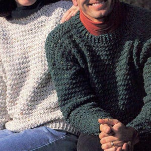 Peut inclure: Deux pulls en tricot texturé. L'un est de couleur crème clair, l'autre est vert foncé. Les pulls ont un col rond et des manches longues. L'image montre les pulls de la poitrine vers le haut.