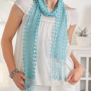 May include: A light blue, open-weave scarf with fringe detail. The scarf is draped over a white top and is made of a delicate, possibly crocheted, material. The scarf's color is a soft, pastel blue.