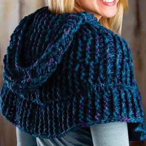 Puede incluir: Un chal de punto azul turquesa con capucha y detalles en morado. El chal está hecho con un hilo grueso y tiene un corte holgado y fluido.