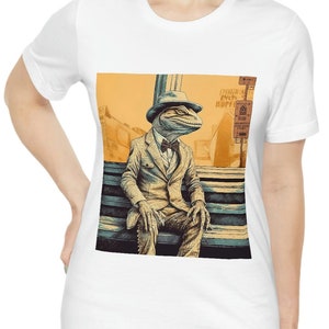 May include: A white short-sleeve t-shirt featuring a graphic print of a lizard wearing a suit, bow tie, and fedora, sitting on a bench. The illustration uses shades of orange, blue, and black, with a street sign visible in the background.