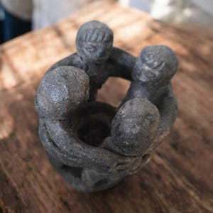 Puede incluir: Un grupo de cuatro pequeñas figuras de cerámica negra que se toman de la mano en un círculo. Las figuras son estilizadas y tienen rasgos simples.